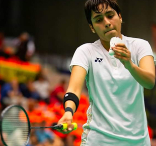 A woman confidently holds a racket and ball, ready for badminton game wearing casual white sportswear
