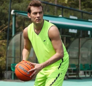A man in a vibrant green sports tshirt confidently holds a basketball, showcasing his passion for the sport