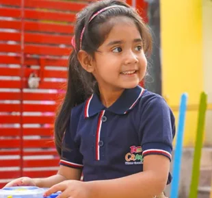 A young girl, dressed in a school house uniform, gently holds a toy in her hands, radiating innocence and joy