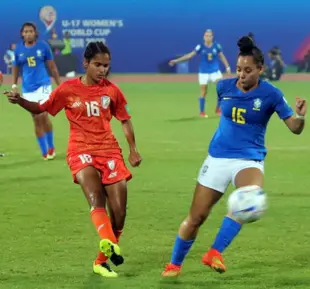 Two female football opponents, one wearing red and the other wearing blue sports jerseys, are playing on the ground