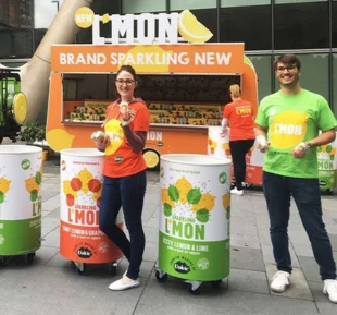 Two individuals standing beside a lemon vending machine, ready to purchase refreshing beverage with promotional wear