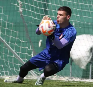 A person in a blue jersey skillfully catches a soccer ball during a game, displaying agility and precision