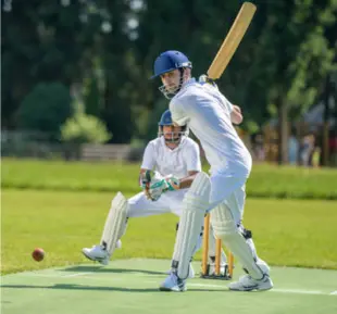 A man in white jersey and helmet playing cricket on a field, showcasing his skills and passion for the sport
