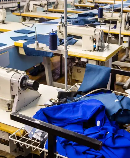 A factory floor filled using blue garments with numerous sewing machines manufacturing blue sports uniforms