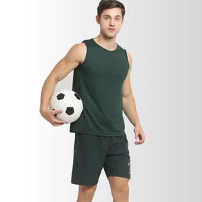 A young man is getting ready for his game while showcasing his green jersey, green shorts, and football in his hand.