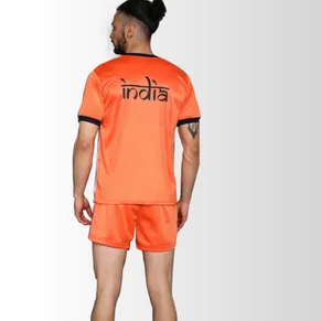 A man standing in a sports uniform of an orange sports jersey with the name India on the back, paired with orange shorts