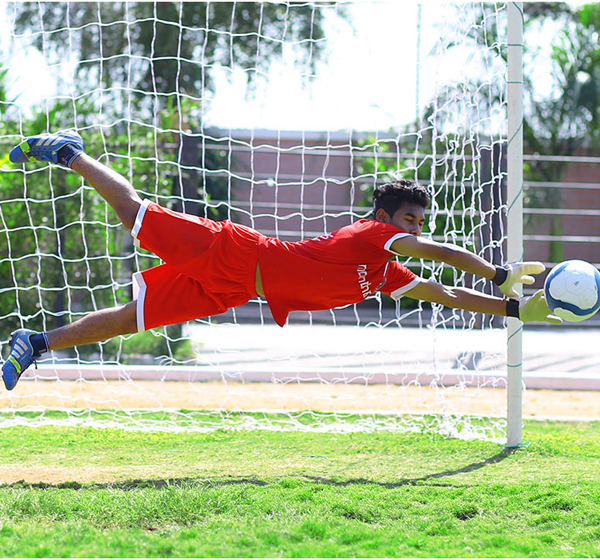 A football player leaps high to seize the ball mid-air during a game with casual sports uniform & shoes